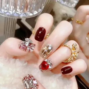Close-up of burgundy plaid heart crystal press-on nails on hand