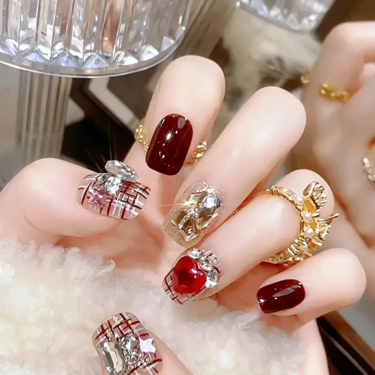 Close-up of burgundy plaid heart crystal press-on nails on hand